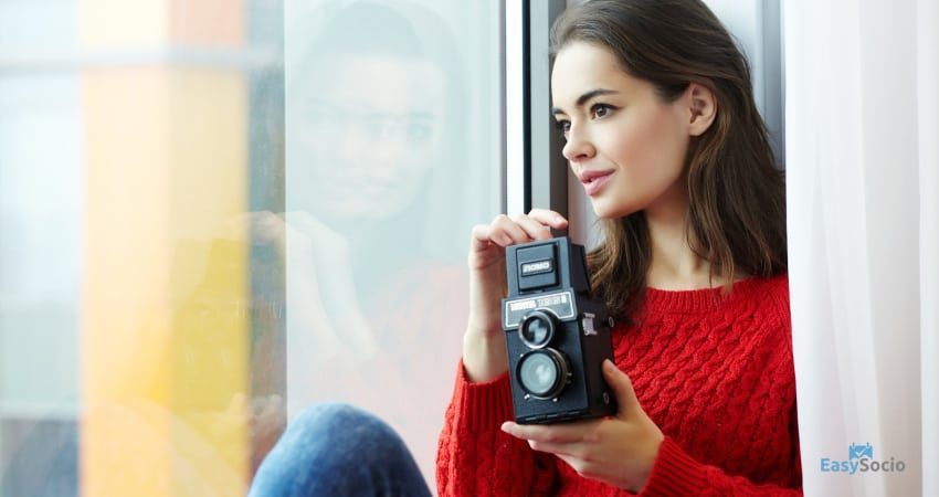 girl posing for a picture near a window holding a camera